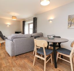 A living room with a dining table and chairs and a sofa at The Old Cowshed in Broadwoodwidger near Lifton
