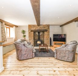 A living room with patterned armchairs a coffee table a stone fireplace and a television at Bunts Barn Northlew near Hatherleigh