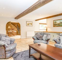 A living room with patterned sofas wooden coffee table and a dining area visible through an archway at Bunts Barn in Northlew near Hatherleigh
