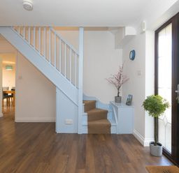 An entryway with wooden flooring a black front door light blue staircase and small potted plants at Spernenwyn in St Ives