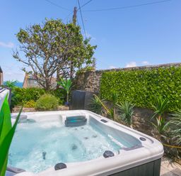 An outdoor hot tub surrounded by plants and a stone wall at Spernenwyn in St Ives
