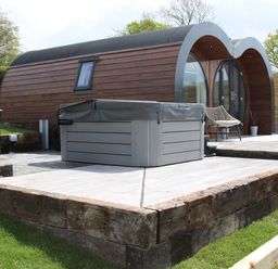 An outdoor patio area with a hot tub and chair next to a rounded wooden cabin at Ceunant in Llanfihangel-y-Creuddyn near Aberystwyth