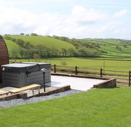 An outdoor hot tub on a paved area with a wooden bench and green fields in the background at Ceunant Llanfihangel-y-Creuddyn near Aberystwyth
