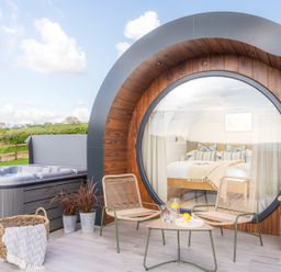 Outdoor patio area with two chairs a table a hot tub and large circular window showing a bedroom at Ceunant in Llanfihangel-y-Creuddyn near Aberystwyth