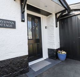 The front door entrance with a doormat and flower pot next to a black gate at Harvenna Cottage in Crackington Haven