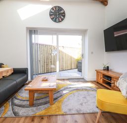 A living room with a black sofa yellow chair wooden coffee table and wall clock with glass door to outside at Harvenna Cottage in Crackington Haven