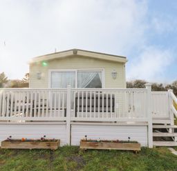 A small beige house with a white wooden porch and railing in a grassy area at Park Lane in Llanteg near Kilgetty