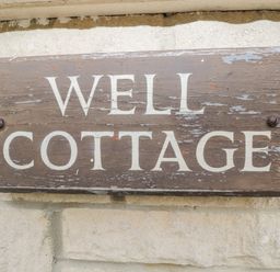 A wooden sign with the text Well Cottage mounted on a stone wall at Well Cottage Nr Malmesbury