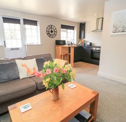 A living room with a sofa and a kitchen area at Well Cottage Nr Malmesbury