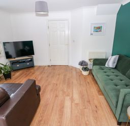 A living room with a green sofa and leather armchair a television on a stand and a wooden floor at 12 Clos Yr Wylan in Barry