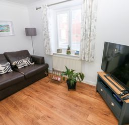 A living room with a brown leather sofa two patterned cushions a floor lamp a window with curtains a plant a tv on a stand and a magazine rack at 12 Clos Yr Wylan in Barry