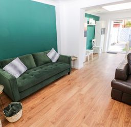 A living room with green and brown sofas and wooden flooring leading to a dining area and garden at 12 Clos Yr Wylan in Barry