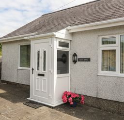 A front entrance with a white door and porch a potted plant with pink flowers on the ground near a window and a sign reading Glan Awel at Glan Awel in Nefyn