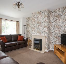 A living room with dark brown leather sofas a fireplace a wooden TV stand with a TV and floral wallpaper at Glan Awel in Nefyn