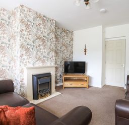 A living room with a fireplace floral wallpaper two brown sofas and a television on a wooden stand at Glan Awel in Nefyn