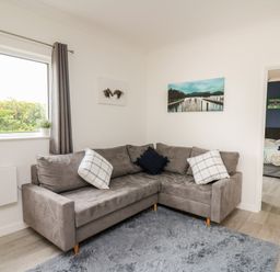 A living room with a grey sectional sofa and two paintings on the wall at Ty Cariad in Llangynin near St Clears