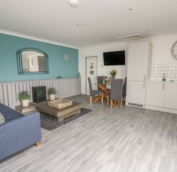 A room with a blue sofa and coffee table blue wall with a mirror dining table with chairs and kitchenette with white cabinets at Ty Cwtch in Llangynin near St Clears