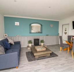 A living room with a blue sofa a wooden coffee table and a dining area with a glass table and gray chairs at Ty Cwtch in Llangynin near St Clears