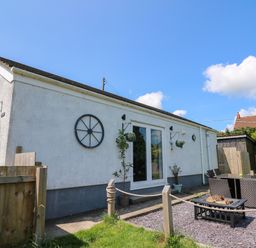 A white exterior wall of a house with hanging plants a glass door outdoor seating and firepit in a fenced garden area at Ty Cwtch in Llangynin near St Clears