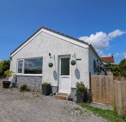 A small white house with green plants in pots and a wooden fence at Ty Cwtch in Llangynin near St Clears