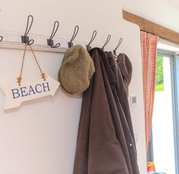 An entrance with a coat rack, a hat, and a beach sign at Carines Barns - Tre, Cubert