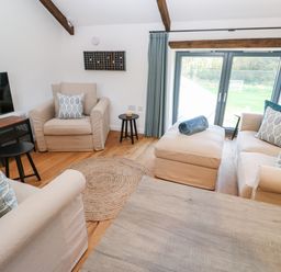 A living room with beige armchairs a sofa a round rug a wooden table and a TV at Carines Barns - Pol in Cubert