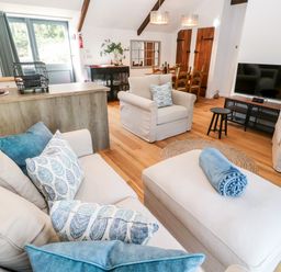 A living room with beige sofas and blue pillows a dining table and television at Carines Barns - Pol in Cubert