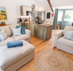 A living area with beige sofas and blue cushions near a kitchen island with wooden floors at Carines Barns - Pol in Cubert