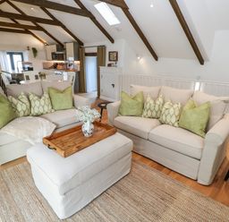 A living room with two beige sofas green cushions a wooden tray on an ottoman and exposed ceiling beams at Carines Barns - Par in Cubert