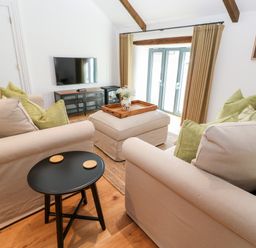 A living room with two beige sofas green pillows a black side table a wooden floor and a television at Carines Barns - Par in Cubert