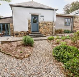 A stone and whitewashed building with a blue door and garden beds surrounded by gravel at Carines Barns - Wesley Barn in Cubert