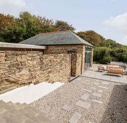 An outdoor patio area with stone steps gravel path wooden seating and a stone building at Carines Barns - Wesley Barn in Cubert