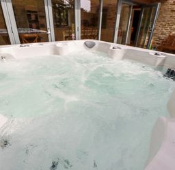 A bubbling hot tub in an outdoor area with stone walls glass doors and a wooden bench at Carines Barns - Wesley Barn in Cubert
