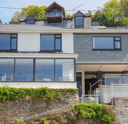 The exterior of a two-story house with large windows and a stone retaining wall at Anjoma in Looe