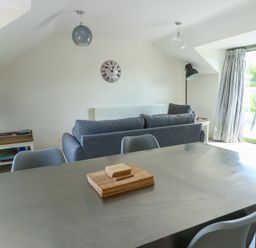 A living area with gray sofa dining table chairs wall clock and sliding glass door at Gwalia Cottage in Brynsiencyn