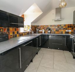 A kitchen with black cabinets gray countertops tiled backsplash and built-in oven at Gwalia Cottage in Brynsiencyn