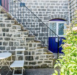 An outdoor stone staircase with a black railing next to a round white table and two white chairs with plants nearby at The Hayloft in St Florence