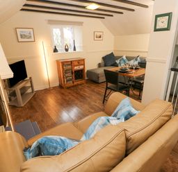 A living room with a beige sofa blue cushions wooden floor dining table and chairs next to a kitchen with a washing machine at The Hayloft in St Florence