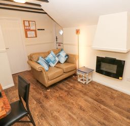 A small living room with a leather sofa blue cushions wall mounted fireplace wooden floor and dining table with chairs at The Hayloft in St Florence