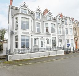 A row of three story terraced houses with bay windows and chimneys on a street at Llwyn Onn in Criccieth