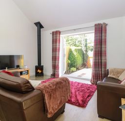 A living room with two brown sofas a fireplace and open doors to a garden at Beck View Weston Longville near Lenwade