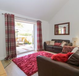 A living room with brown leather sofas and red rug near patio doors at Beck View Weston Longville near Lenwade