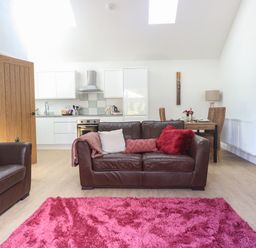 An open plan living room and kitchen with brown leather sofas a pink rug a wooden dining table and chairs white kitchen cabinets and wooden door at Beck View Weston Longville near Lenwade