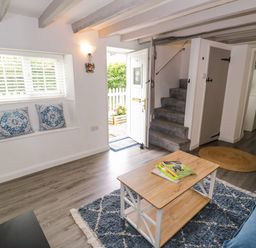 A living room with a sofa, table, and stairs at The Cottage in Ettington