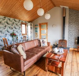 A living room with a brown leather sofa wooden coffee table and a wood burning stove at Y Caban Glas in Rhydlewis near Brynhoffnant