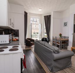 A kitchen with a stove and microwave next to a living area with a sofa chairs dining table and wall mounted television at Beach in Bridlington