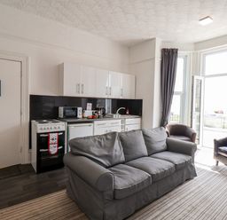 A living room with a gray sofa two armchairs kitchenette and a door to a balcony at Beach in Bridlington