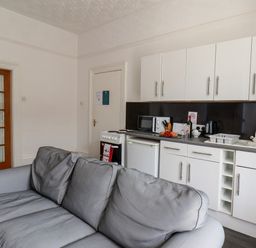 A kitchen with white cabinets a countertop appliances and a gray sofa in front at Beach in Bridlington