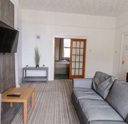 A living room with a grey couch a wall-mounted TV a small wooden table and a side table with plants at Beach Bridlington
