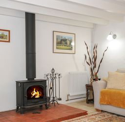 A living room with a wood burning stove a sofa with cushions and a throw and framed pictures on the wall at Henwood Barn in Henwood near Upton Cross